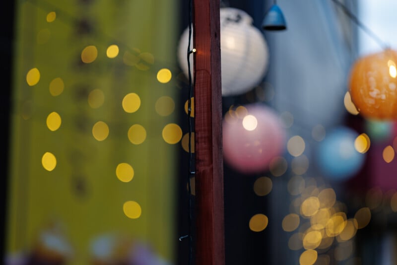 A close-up of a wooden pole with string lights, set against a blurred background of glowing lanterns and yellow bokeh lights, creating a festive and atmospheric scene.