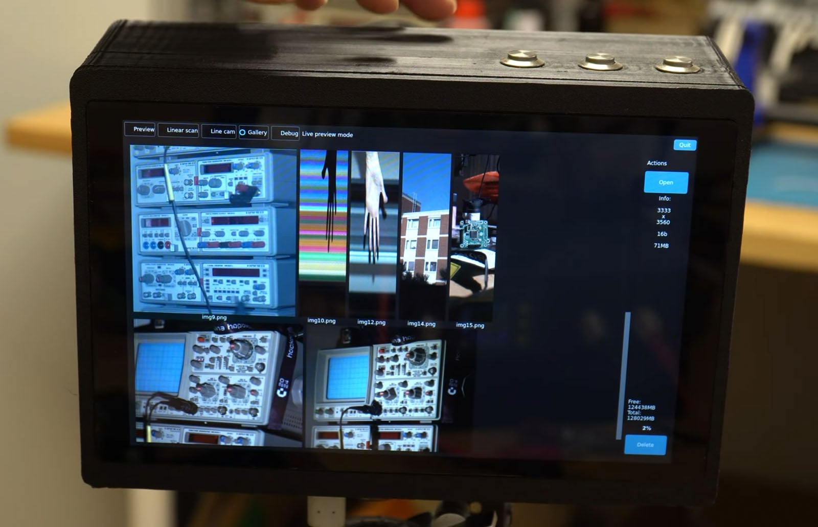 A close-up of a touchscreen device displaying a gallery of various images, including electronics and circuit boards, with control buttons and a settings menu visible on the screen.