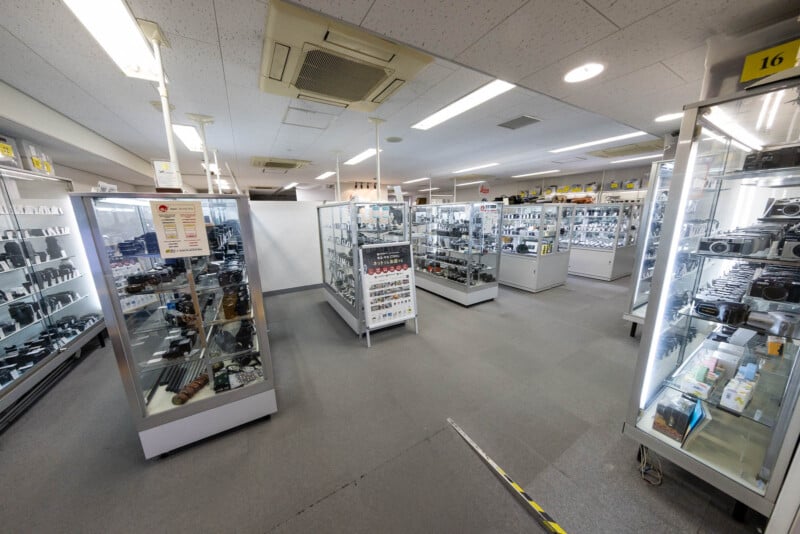 A well-lit store interior with glass display cases filled with cameras and photography equipment, arranged neatly on shelves, with an aisle for customers to walk through.