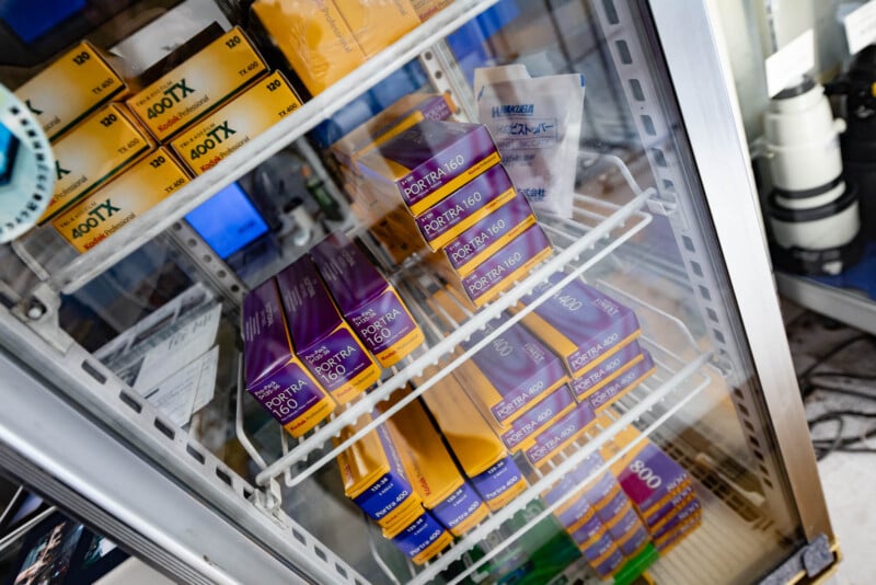 Shelves of a refrigerator filled with boxes of Kodak Portra and other film rolls, primarily in purple and yellow packaging, viewed from above through the glass door.
