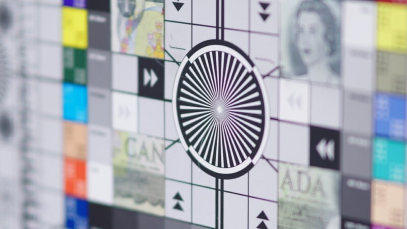 A close-up of a TV test pattern with a central black and white radial design, grayscale squares, arrows, and blurred images of people and text in the corners.