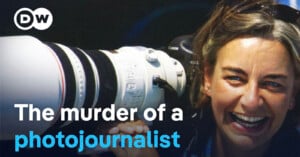 A woman with sunglasses on her head smiles while holding a large camera lens. The text on the image reads: "The murder of a photojournalist." The DW logo is in the top left corner.