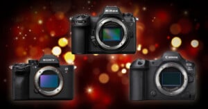 Three mirrorless digital cameras—Sony, Nikon, and Canon—are displayed against a blurred background of festive red and yellow lights. Each camera’s lens mount and sensor are visible.