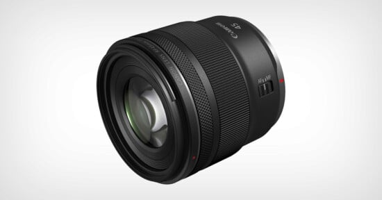 A black Canon RF 50mm camera lens is shown angled slightly to the left on a plain white background. The lens features textured focus rings and a red alignment dot near the mounting end.