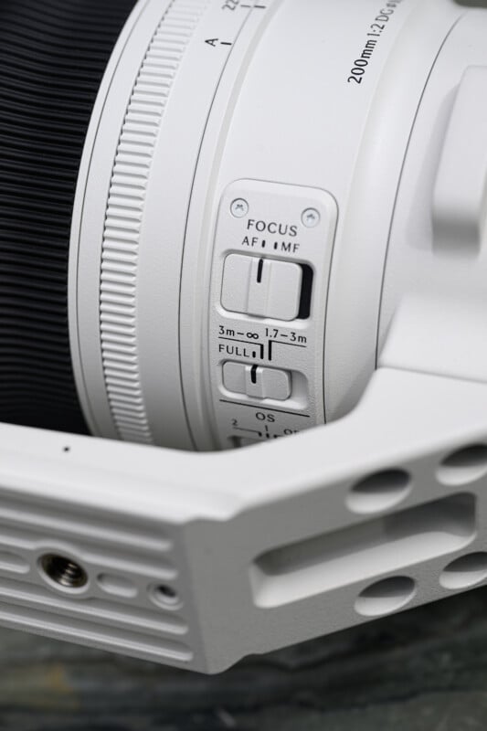 Close-up of a white camera lens showing focus mode switches and distance settings labeled "FOCUS AF | MF," "3m–∞," "1.7–3m," "FULL," and "OS" on the side.