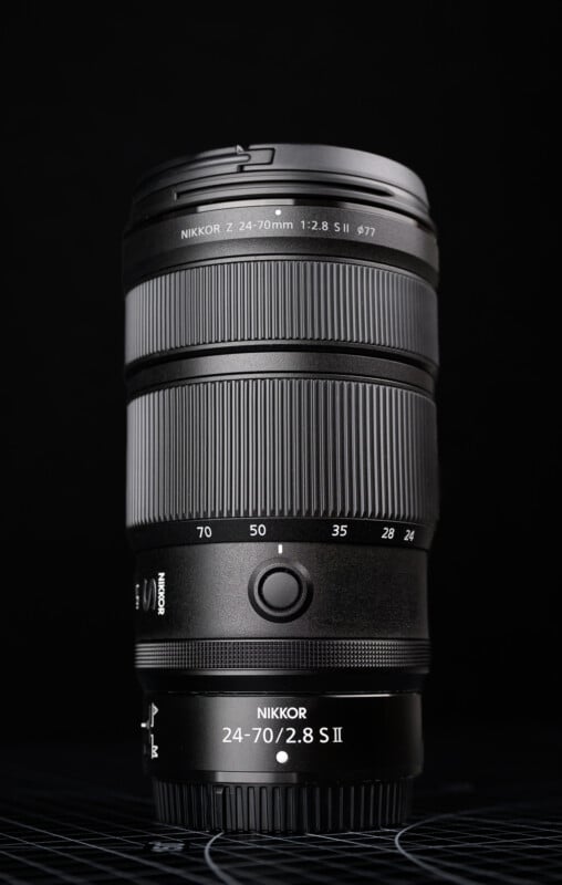 A black Nikon NIKKOR Z 24-70mm f/2.8 S II camera lens stands upright against a dark background, with clear markings for focal lengths and aperture settings visible.