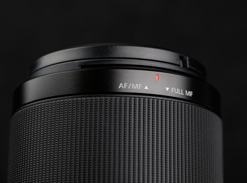 Close-up of a camera lens showing a textured grip and a switch labeled "AF/MF" and "FULL MF" with a small red marking, set against a dark background.