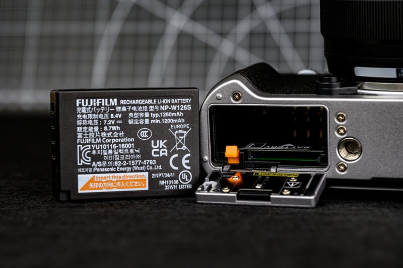 A close-up of a Fujifilm camera next to an open battery compartment and a Fujifilm rechargeable lithium-ion battery with visible labels and specifications.