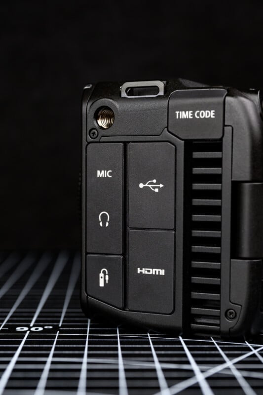 Close-up of a camera or audio device showing ports labeled TIME CODE, MIC, USB, headphone, and HDMI, with a textured black and white grid surface underneath and a dark background.