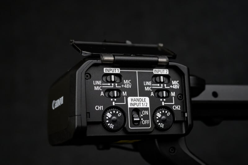 Close-up of the audio input controls on a Canon camera, showing dials and switches for adjusting input channels, mic/line levels, +48V phantom power, and handle input. The background is dark and out of focus.