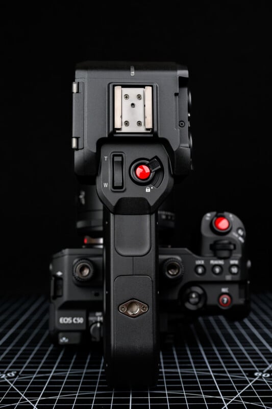 A Canon EOS C50 cinema camera is shown from above and behind, highlighting its top handle, various buttons, and a lens, all set against a black background with a grid surface below.