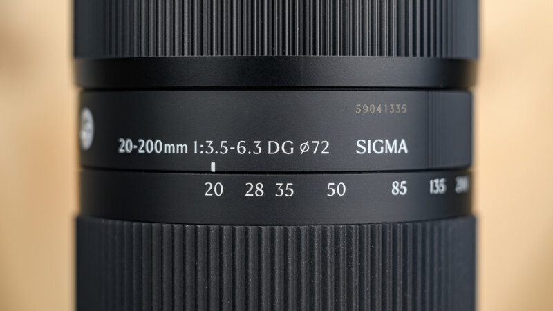 Close-up of a Sigma camera lens showing focal lengths from 20mm to 200mm, aperture range 1:3.5-6.3, and a 72mm filter thread size, with fine textured focus and zoom rings.