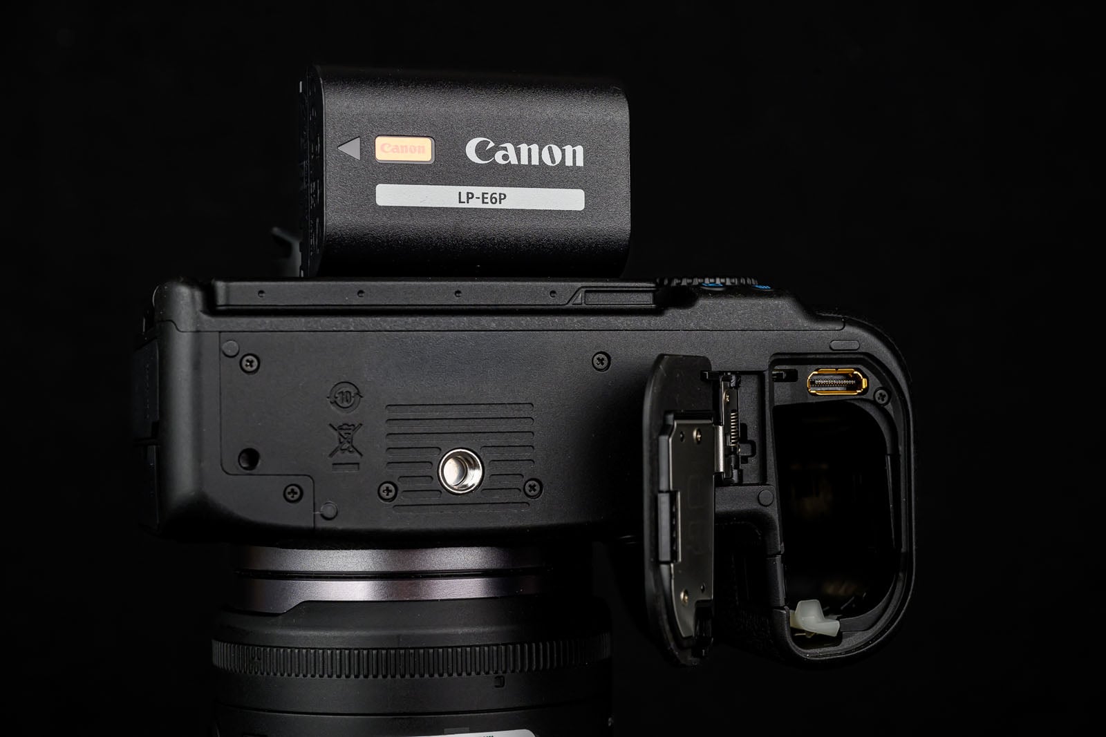 Close-up of a Canon camera with the battery compartment open and a Canon LP-E6N battery partially inserted, against a black background.