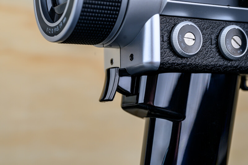 Close-up of a vintage black and silver camera, showing part of the lens, textured body, and two round control dials against a blurred beige background.
