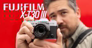 A person holding a Fujifilm X-T30 III camera in front of their face, with a red background and the text "FUJIFILM X-T30 III" beside them.