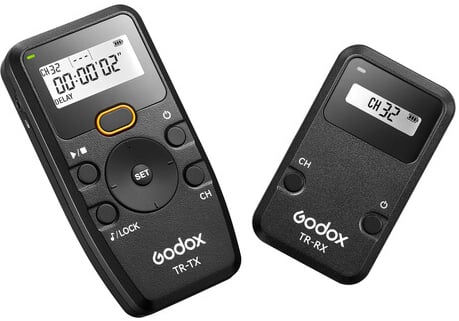 Two black Godox wireless remote devices, model TR-TX (transmitter) and TR-RX (receiver), with digital displays showing channel 32. Both have buttons for controls and branding visible on the front.