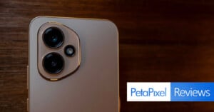 Close-up of a smartphone's rear camera module with two large lenses and a small sensor, placed on a wooden surface. The Petapixel Reviews logo appears in the bottom right corner.
