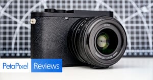 A Leica digital camera with a large lens is displayed on a surface, in front of a geometric black-and-white background. The image includes "PetaPixel Reviews" text in the lower left corner.