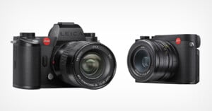 Two black Leica digital cameras with prominent lenses and red Leica logos are shown side by side on a white background; one camera is larger with a viewfinder, and the other is more compact.