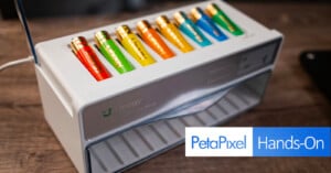 A white battery charger with eight color-coded AA rechargeable batteries inserted. The charger is labeled “ingay.” The foreground features a “PetaPixel Hands-On” graphic.