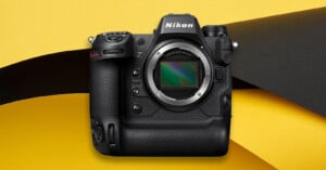 A Nikon mirrorless camera body without a lens is displayed against a yellow and black abstract background.