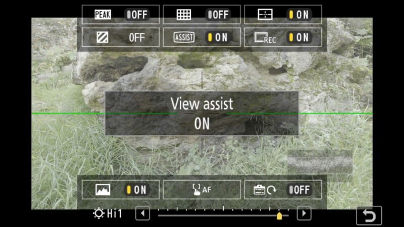 A camera screen displays various settings with "View assist ON" in the center. The background shows grass and rocks, and camera interface icons line the top and bottom of the screen.
