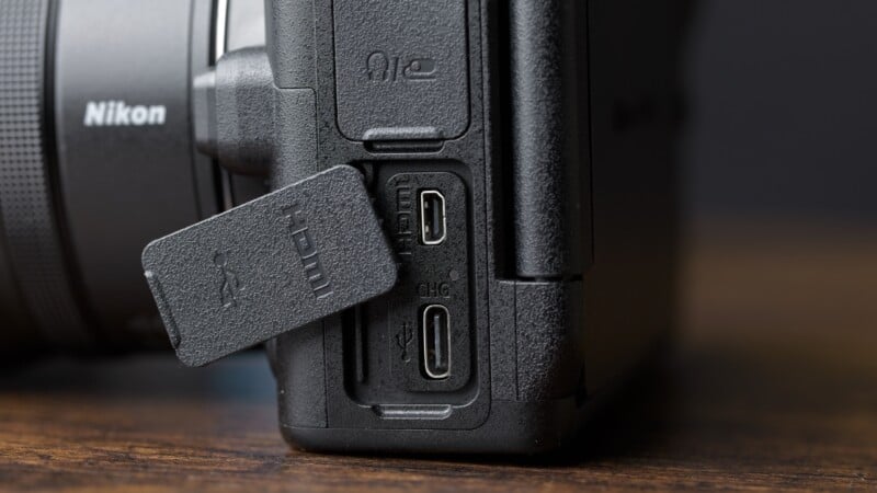 Close-up of a Nikon camera’s side ports, showing open rubber cover revealing micro HDMI and USB-C ports on a wooden surface.