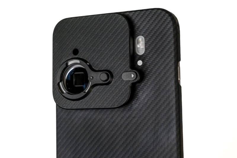 A close-up of a smartphone with a textured black case and a protective cover partially blocking the camera lens and flash on the back.