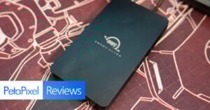A black OWC Envoy Ultra external drive rests on a detailed, red and white illustrated desk mat. The bottom left corner displays "PetaPixel Reviews" in white and blue text boxes.