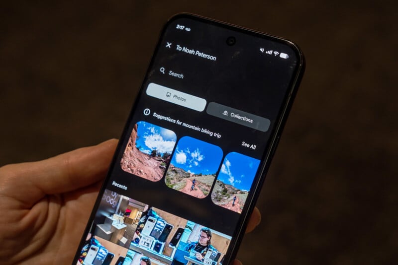 A hand holds a smartphone displaying a photo gallery app with biking trip suggestions, including images of scenic trails and blue skies, under a section labeled “To Noah Peterson.”.