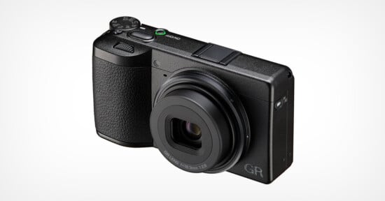 A black compact digital camera with a textured grip, prominent lens, and control buttons on the top, displayed on a plain white background.