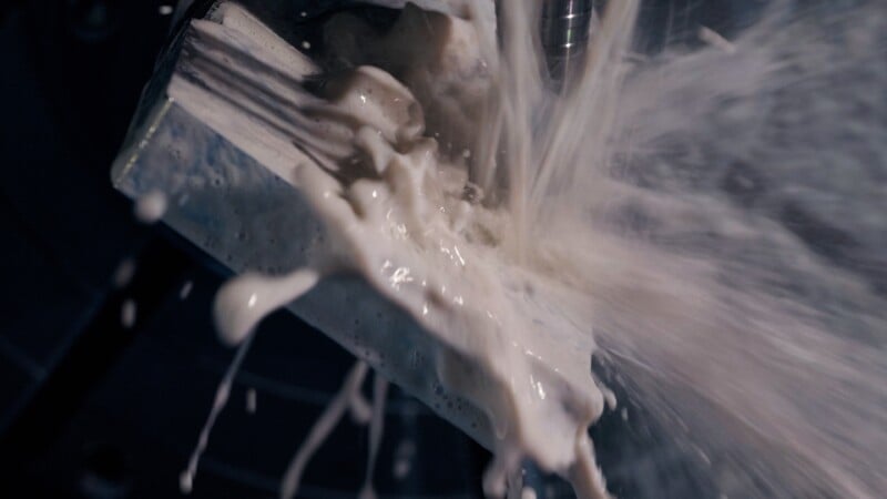 Close-up of a metal part being machined with coolant fluid splashing intensely, capturing the dynamic motion and interaction between the tool and metal surface.