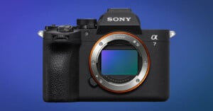 A Sony Alpha 7 mirrorless digital camera body is shown facing forward, displaying its large sensor and lens mount, against a blue gradient background.