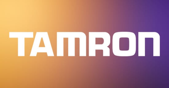 The image features the word "TAMRON" in bold, white uppercase letters centered on a gradient background that transitions from orange on the left to purple on the right.