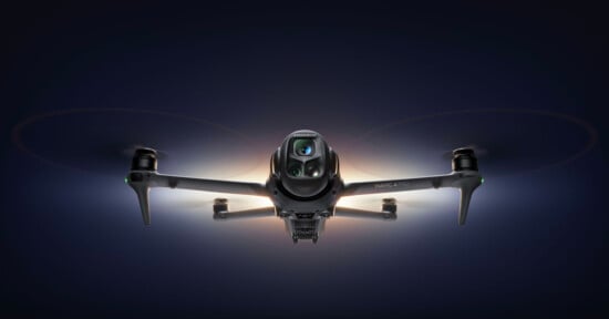 A front-facing view of a quadcopter drone, the DJI Mavic 3 Pro, with glowing lights highlighting its camera and rotors, set against a dark background.