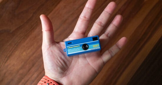 A person holds a tiny blue Kodak toy camera in their palm, with a wood surface in the background.