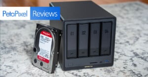 A black four-bay network attached storage device sits on a carpet next to a 4TB hard drive. A “PetaPixel Reviews” banner appears in the upper left corner of the image.