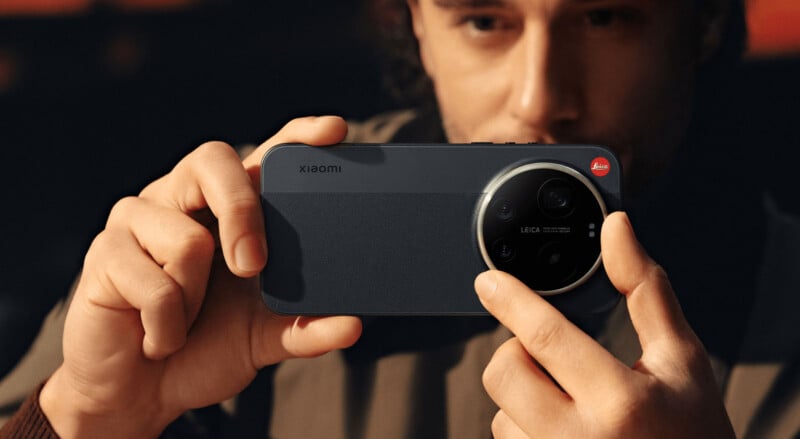 A person holds a Xiaomi smartphone horizontally, with the camera and Leica branding visible on the back, as if preparing to take a photo. The individual is partially out of focus in the background.