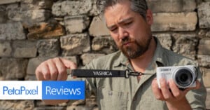 A man in a green shirt holds a white Yashica camera and camera strap outdoors, examining the strap closely. The background is a stone wall. "PetaPixel Reviews" is overlaid at the bottom left.